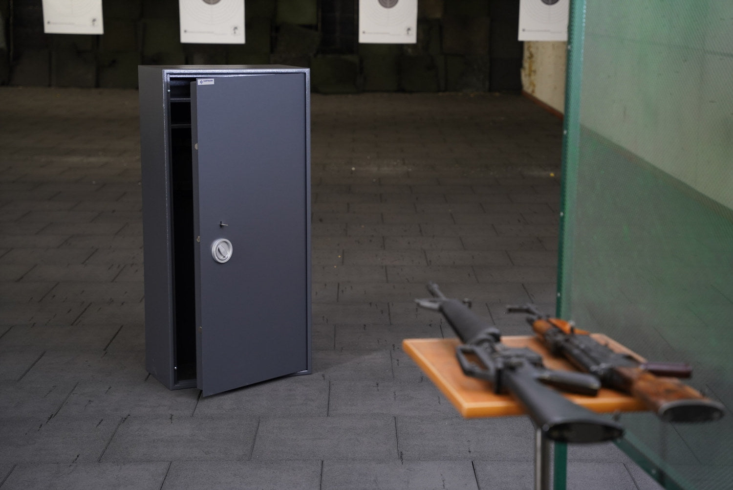 zdjęcie przedstawia dwa karbiny M16 i kałasznikow na stole na strzelnicy obok szafy na broń, w tle widać tarcze strzelnicze